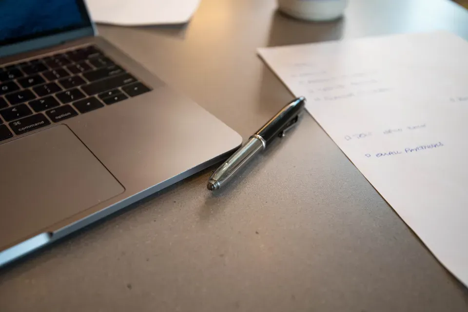 Laptop with handwritten notes and a pen on a desk